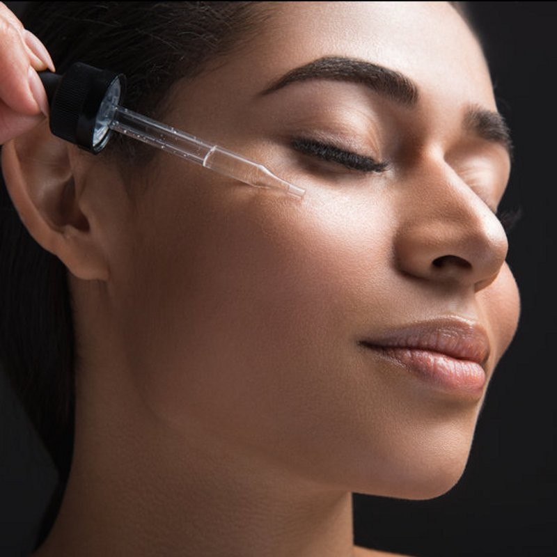 A model with glowing skin applies a drop of Scenturie's Bakuchiol Serum to her cheek.