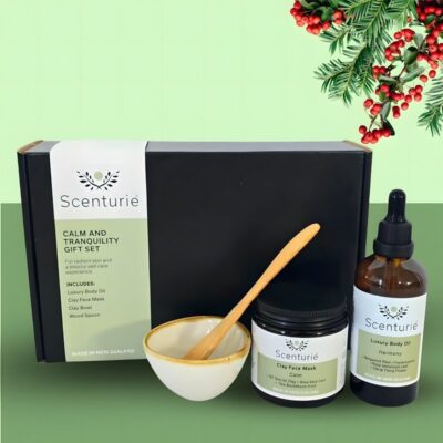 Scenturie's Calm & Tranquility Gift Set, featuring natural aromatherapy body oil, clay face mask, bowl and spoon, set with green background and festive mistletoe.
