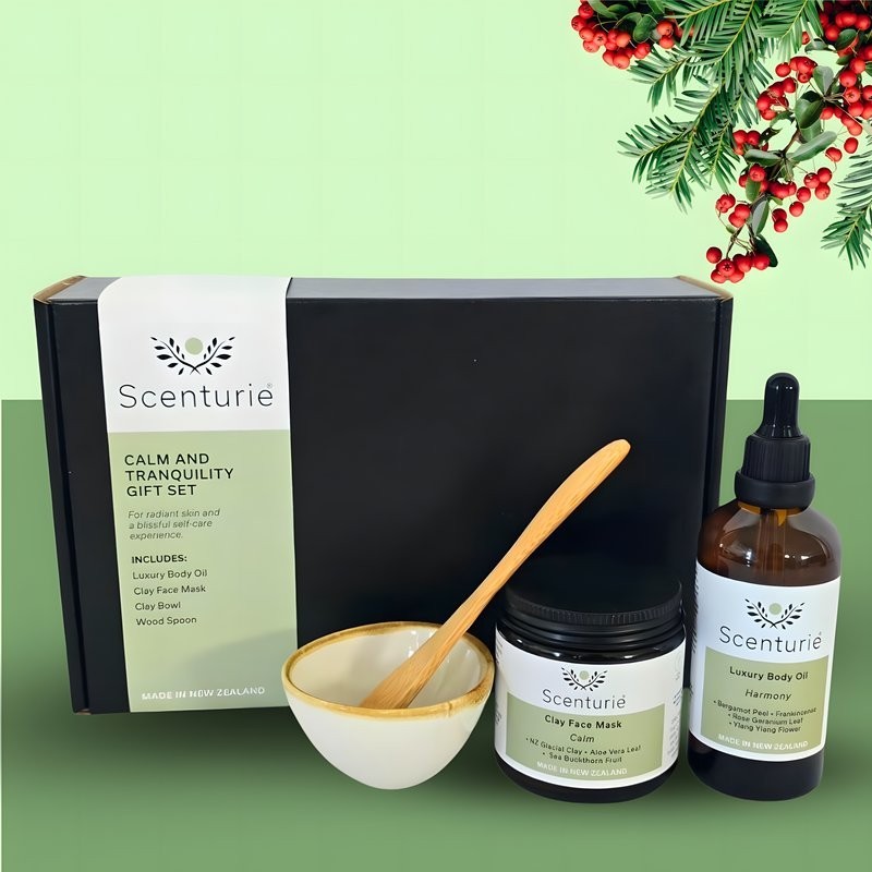 Scenturie's Calm & Tranquility Gift Set, featuring natural aromatherapy body oil, clay face mask, bowl and spoon, set with green background and festive mistletoe.