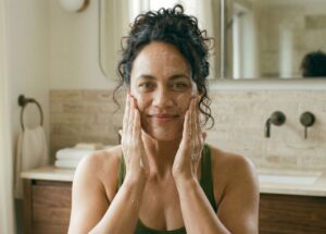 A woman in a natural bathroom setting applying a botanical cleanser, demonstrating the first step of a science-led skincare routine for healthy skin.