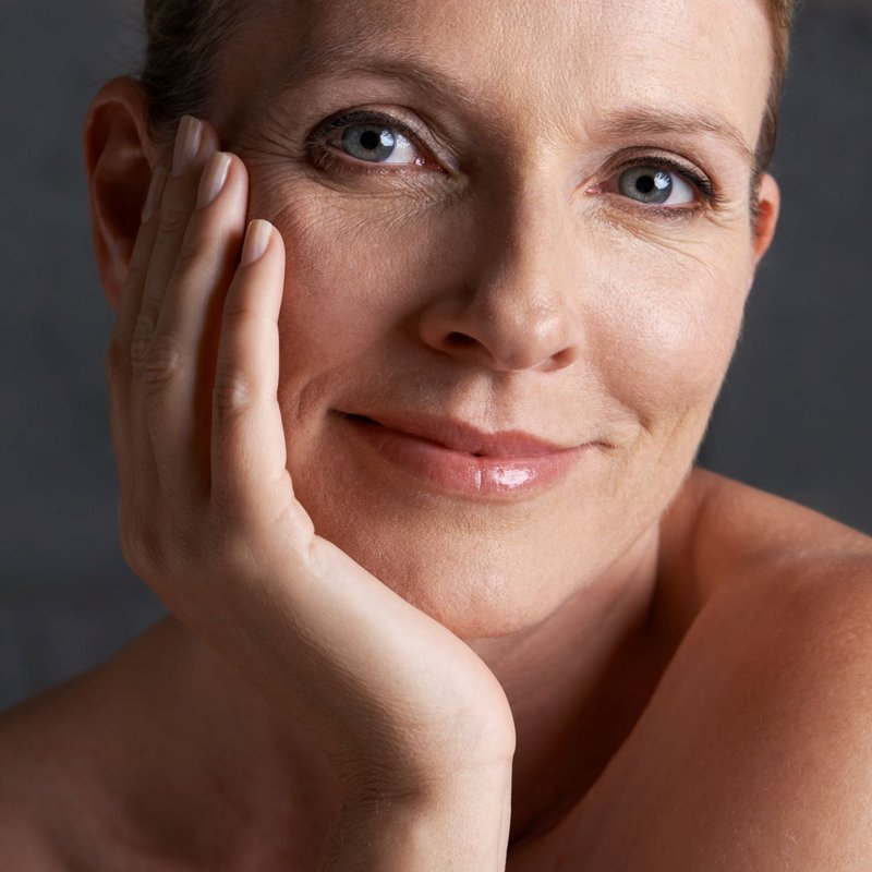 A naturally radiant, smiling woman gently touching her dry skin, representing the journey toward a deeply hydrated, healthy complexion.
